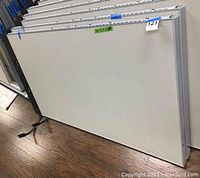 Photo of two stacked office cubicle partition panels from a front view showing large light gray panel surfaces with aluminum edges and labels.