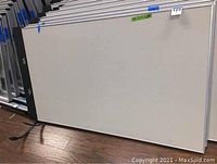 Front view of one beige fabric office cubicle partition showing flat panel surface and metal frame, lying flat on wood floor.