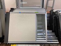 Stacked aluminum framed office partitions with solid and glass panels lying flat on the floor, showing the beige and transparent panels with metal edges