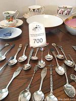 Top view showing collector spoons laid out on a table in front of various china cups and dishes.