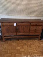Front view of medium finish solid wood sideboard showing five drawers on right and two cabinet doors on left.