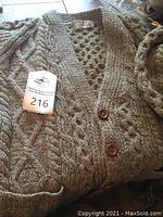 Close-up photo of grey Aran wool sweater with button front and cable knit pattern