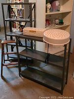 Three metal shelving units along with two white air-dryer units and a small wooden folding step ladder placed on a basement concrete floor.