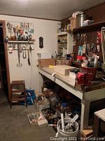 Wide view of workbench area showing bench vise mounted on workbench, boxes on bench, various tools and hardware under and around bench
