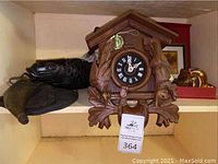 Overall front view of cuckoo clock on shelf alongside carved fish and other decor items.