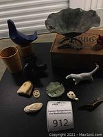 Full view of all lot items showing Art Deco verdigris lily pad dish with frog, various small carved and shaped figurines and knick knacks on black table surface.