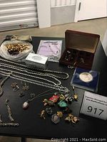 Overview of assorted jewelry on black tabletop including beads, chains, jewelry box, coin, pins, and earrings
