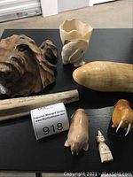 All items arranged on black surface: wooden bear head, alabaster vase, scrimshaw tusk, onyx egg, three small figurines