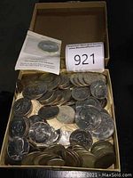 Top-down view of open box showing mixed US Eisenhower dollars and Kennedy half dollars with sealed 1972 Panama five balboas in plastic flip