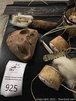 Black engraved wooden panel, carved mask on handle, leather cylinder rattles, round quill bowl partially visible