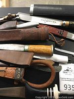 Top view showing multiple cutting tools including knives with different handle materials and sheaths of leather and woven material.
