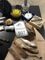 Overview of timers, clock parts, letter openers, carvings, brass tray, glass lamp base and wooden pieces on black surface