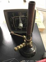Close-up of vintage brass Bunsen burner with mechanical timer behind