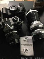 Three cameras and lenses arranged on table: Nikon SLR with lens, Canon compact, telephoto lens and extension ring box