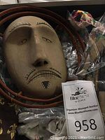 Light wood mask with carved neutral expression, black painted lines and bentwood hoops, packed among peanuts and labeled 958