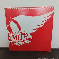 Front album cover showing the Aerosmith winged logo in white on a red background with text 'Aerosmith's Greatest Hits'