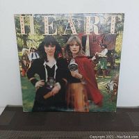 Front cover of the Little Queen album by Heart showing Anne and Nancy Wilson in a forest scene with medieval styling, holding a crystal ball, with album title text.