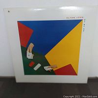 Front view of Elton John 21 at 33 vinyl album cover with abstract colorful artwork featuring poker cards and block colors.