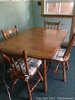 Photo showing the solid maple rectangular kitchen table with four matching spindle back chairs with plaid cushioned chair pads in a corner of a room near window