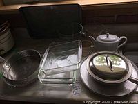 Photo showing stacked glass baking dishes in front of a large black metal tray, with a white ceramic teapot and glass bowls to the side.