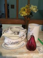 View of Meakin Classic White patterned chinaware including serving platter, lidded sugar bowl, gravy boat, cream pitcher and bowls, plus blown glass items including a red pear and vase with flowers.