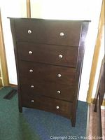 Front view of wooden dresser showing all five drawers and silver knobs.