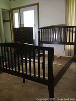 Photo showing the wooden bed frame with headboard and footboard having vertical slats, side rails attached.