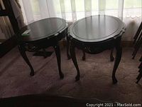 Pair of wooden round end tables with carved details and single drawers.