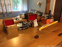 Full view of lot items on wooden surface under window, showing boxes, two clock radios, duster, and jewelry