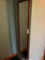 Full view of tall rectangular wood framed mirror showing entire piece hung on wall.