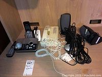 Photo of cordless and corded phones, Dell speakers, and various cables on a wooden surface.