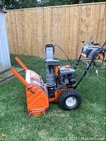 Side view of the orange and black Columbia snow blower showing large tires, engine and chute.