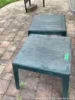 Two green square resin side tables placed on outdoor stone patio surface showing weathered condition.
