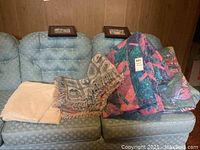 Five bedding items displayed on a blue patterned couch, including plush blanket, cotton throws, and comforters.