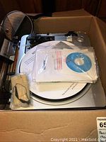Photo of the Memorex record player showing turntable, dust cover, manual and included CD in plastic sleeve inside a cardboard box.