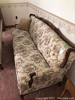 Full length side view of vintage fabric sofa showing floral upholstery and carved wood trim.