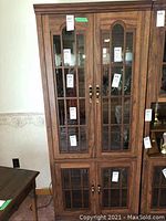 Front closed view of the manufactured wood china cabinet with four glass-paneled doors and brass handles.