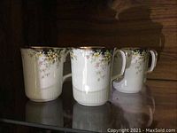 Photo showing a group of four Royal Albert bone china mugs with floral Royal Ascot pattern, gold trim on rim and handles, and ribbed lower exterior.