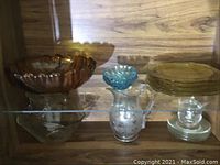 Display shelf with amber footed bowl, blue glass fruit nappies, glass plates and other glassware items
