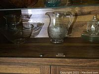 Display of two-tier glass chip bowl, pressed glass pitcher, lidded honey pot, and glass side plates on wooden shelf