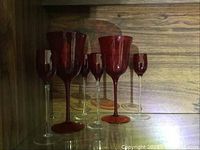 Photo of six ruby red stemware glasses of different sizes on a glass shelf to show the variety in the set.