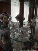 Photo of glass swan figure and angel on glass shelf with floral background
