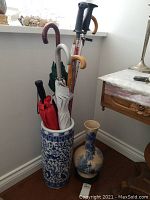 Umbrellas and walking sticks arranged in blue and white ceramic umbrella stand next to two ceramic vases on floor.
