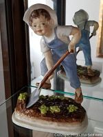 Photo showing the front view of the Royal Worcester figurine of a child in overalls holding a shovel in a garden setting.