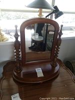 Front view of wooden desk top swivel mirror on scalloped wooden surface with a lamp and couch in background, showing the overall shape and design.