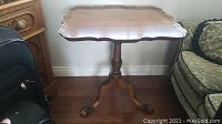 Full view of the solid wood table showing scalloped edge top and claw foot legs.