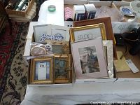 View of various picture frames and framed artworks displayed in boxes on a table.