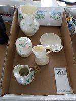 Overview of the five pieces in a cardboard box, showing the Balleek shamrock motif and the broken creamer
