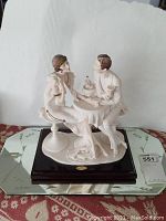 Front view of the ceramic figurine showing couple at table on wooden base