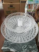 Two centerpiece dishes stacked: larger glass pie plate with looped rim and smaller crystal dish with diamond hobnail pattern.